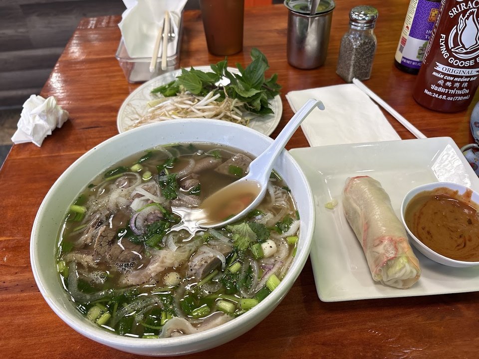 Bowls of pho beside fresh herbs and noodles.